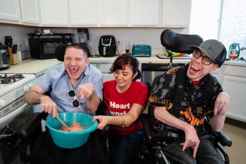 A direct support professional from ALSO teaches two developmentally disabled clients in wheelchairs how to cook for themselves.